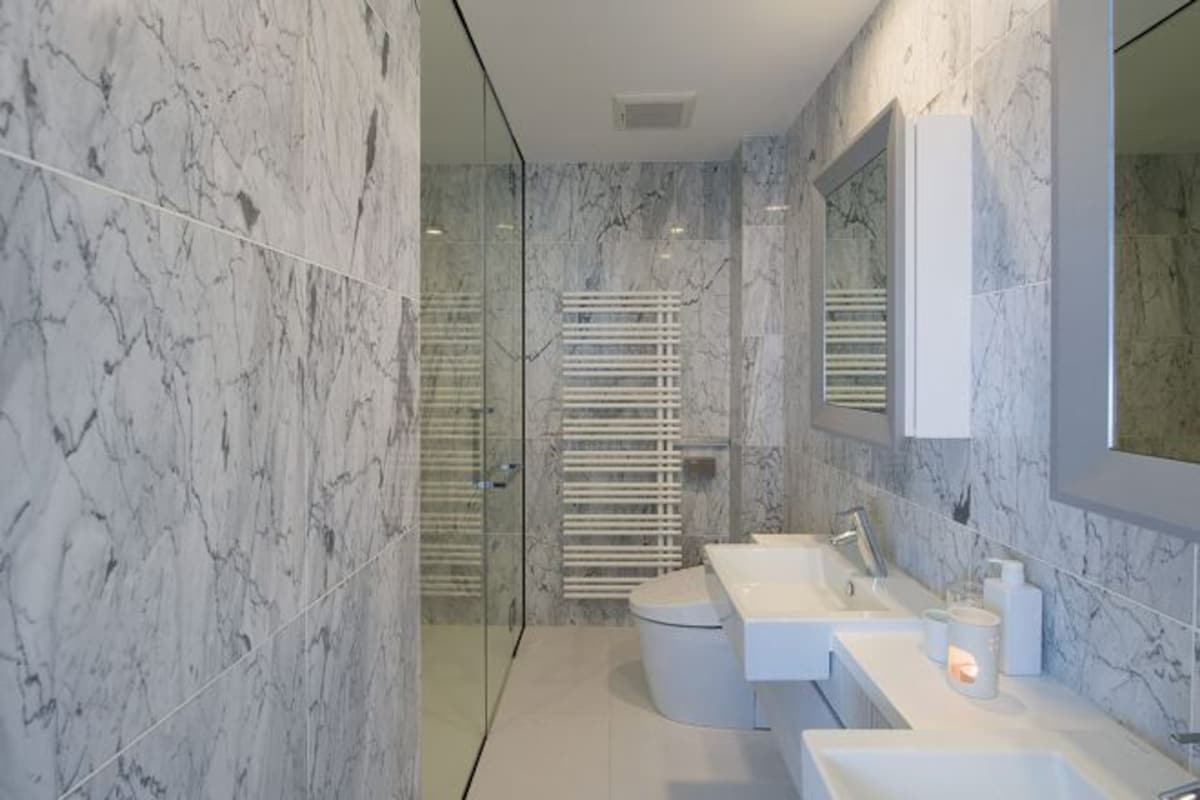 A modern bathroom with marble walls, a glass shower enclosure, and a white vanity with a mirror.