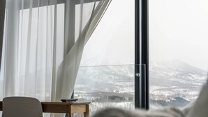 Quarto com vista para uma paisagem nevada através de uma grande janela, uma mesa de cabeceira e uma cadeira.