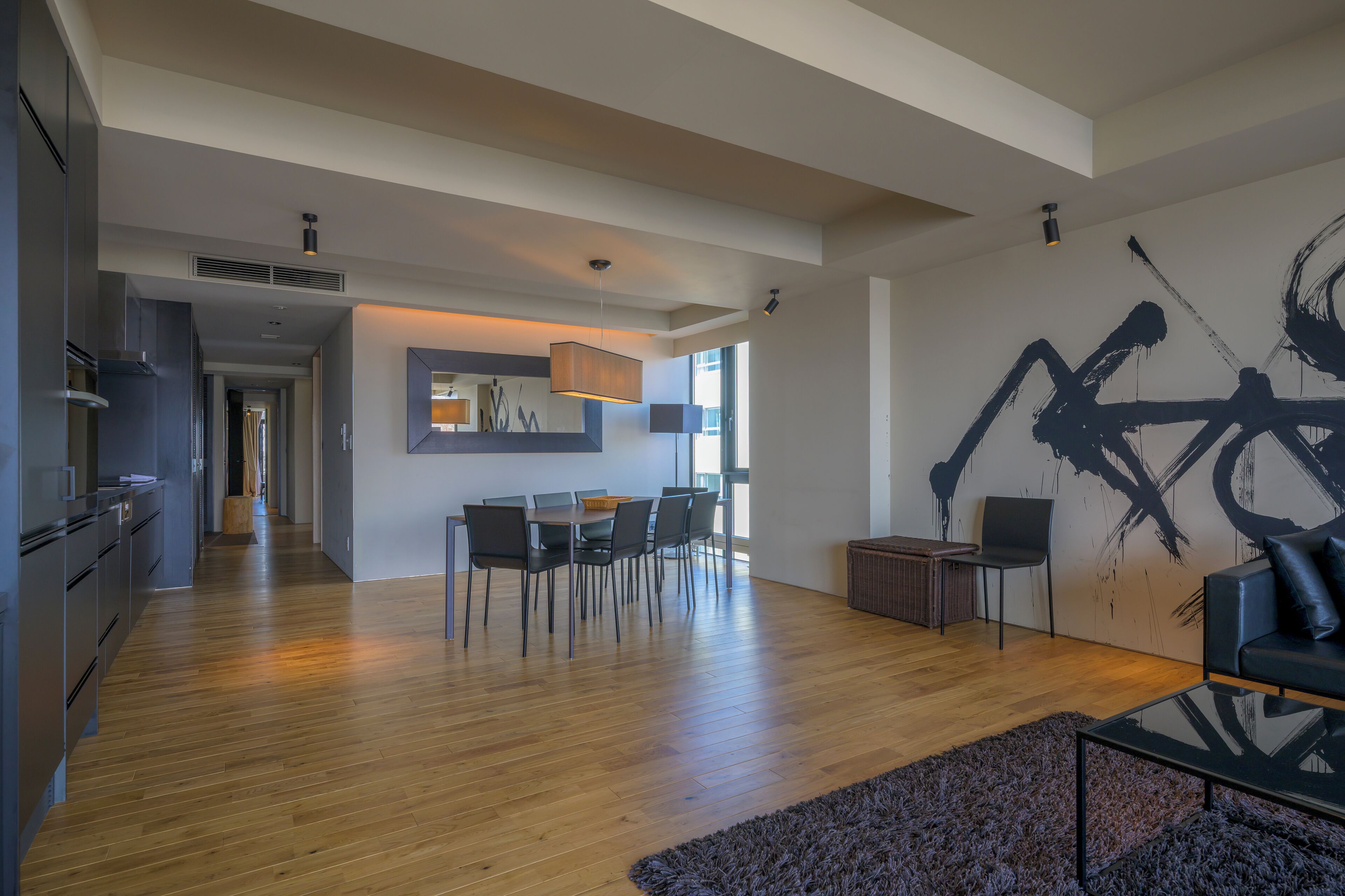 A modern living space with a dining area, kitchen, and a large abstract wall art piece.