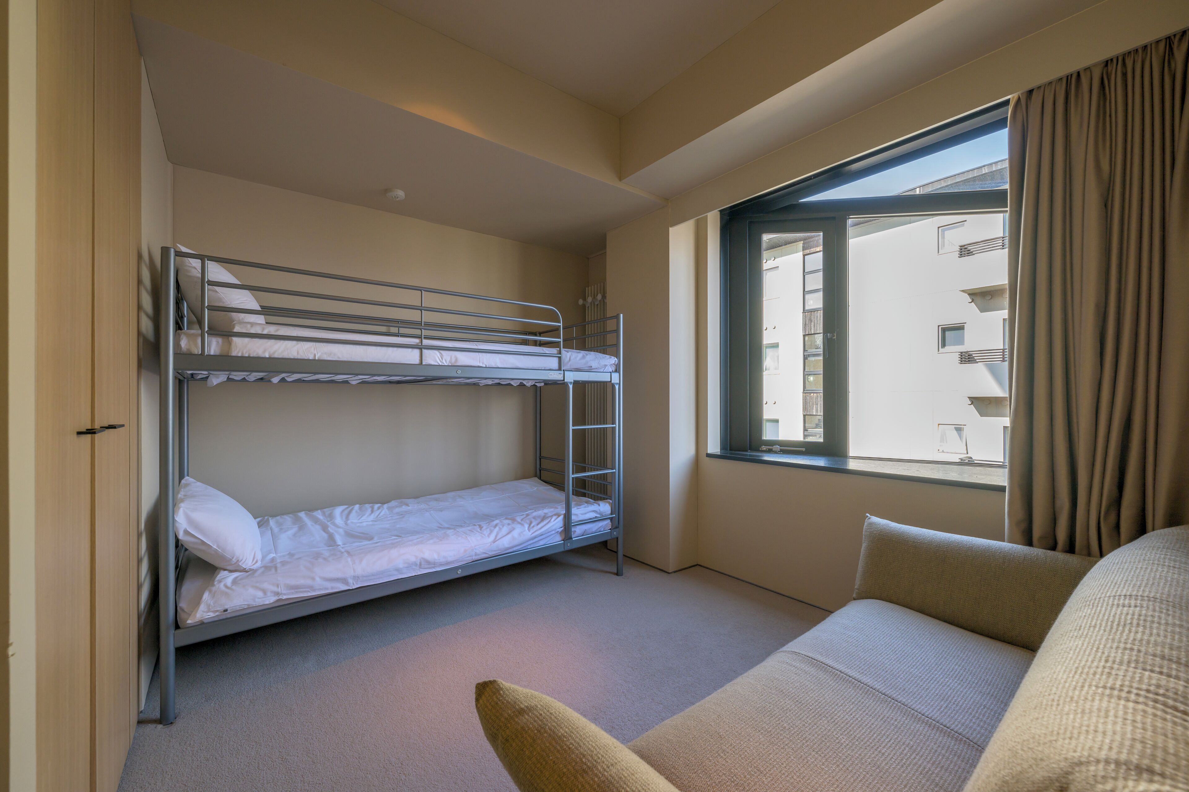 A room with a bunk bed, a sofa, and a window with curtains.