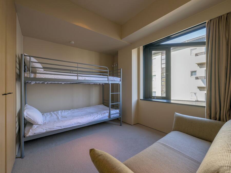 A room with a bunk bed, a sofa, and a window with curtains.
