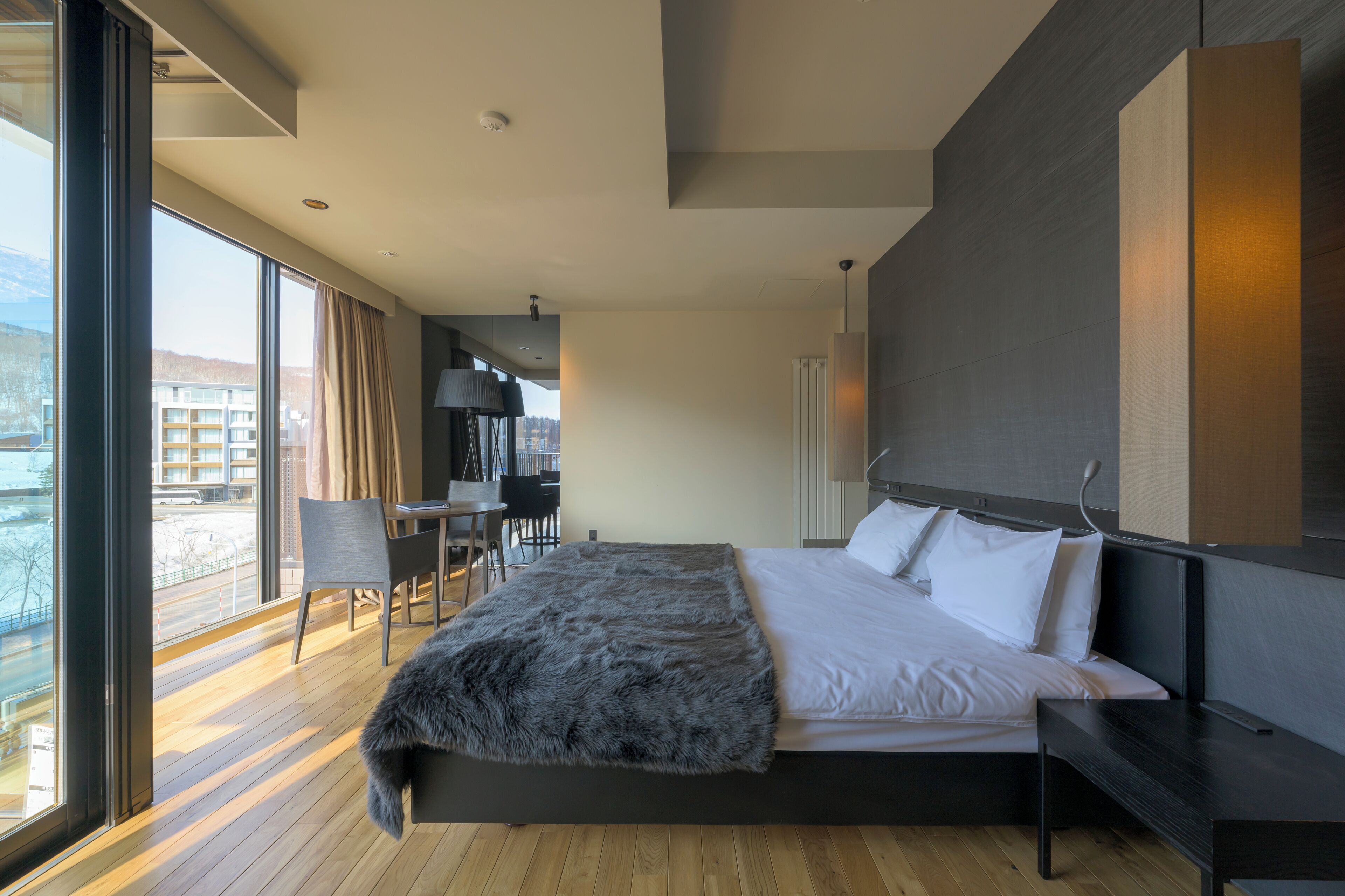 Quarto de hotel moderno com cama grande, vista para a cidade e zona de refeições com cadeiras e mesa.