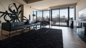 A modern living room with a black sofa, a glass coffee table, and a large abstract painting on the wall. - MUSE Niseko (Kutchan)