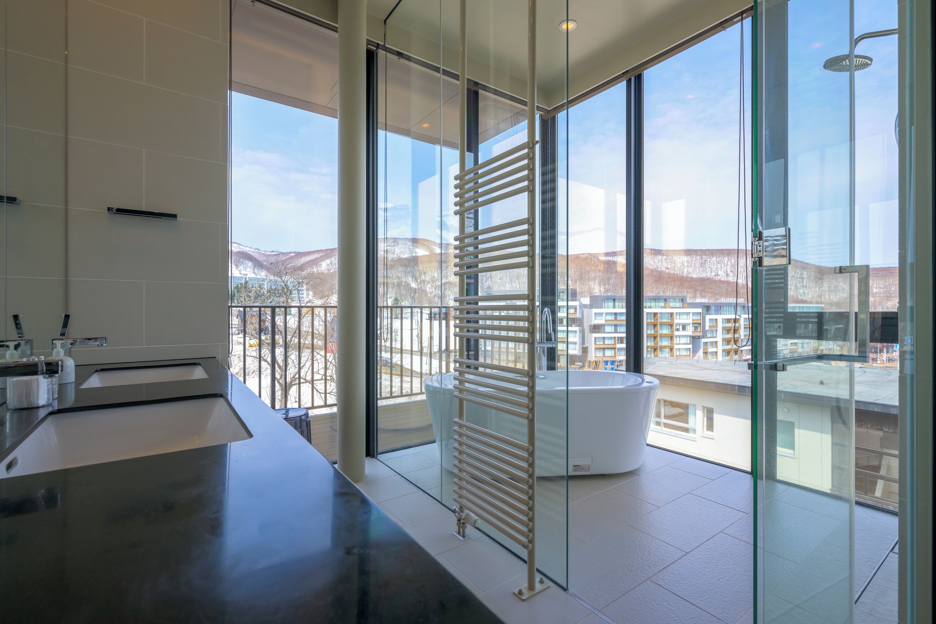 A modern bathroom with a large window, a bathtub, and a glass shower enclosure.