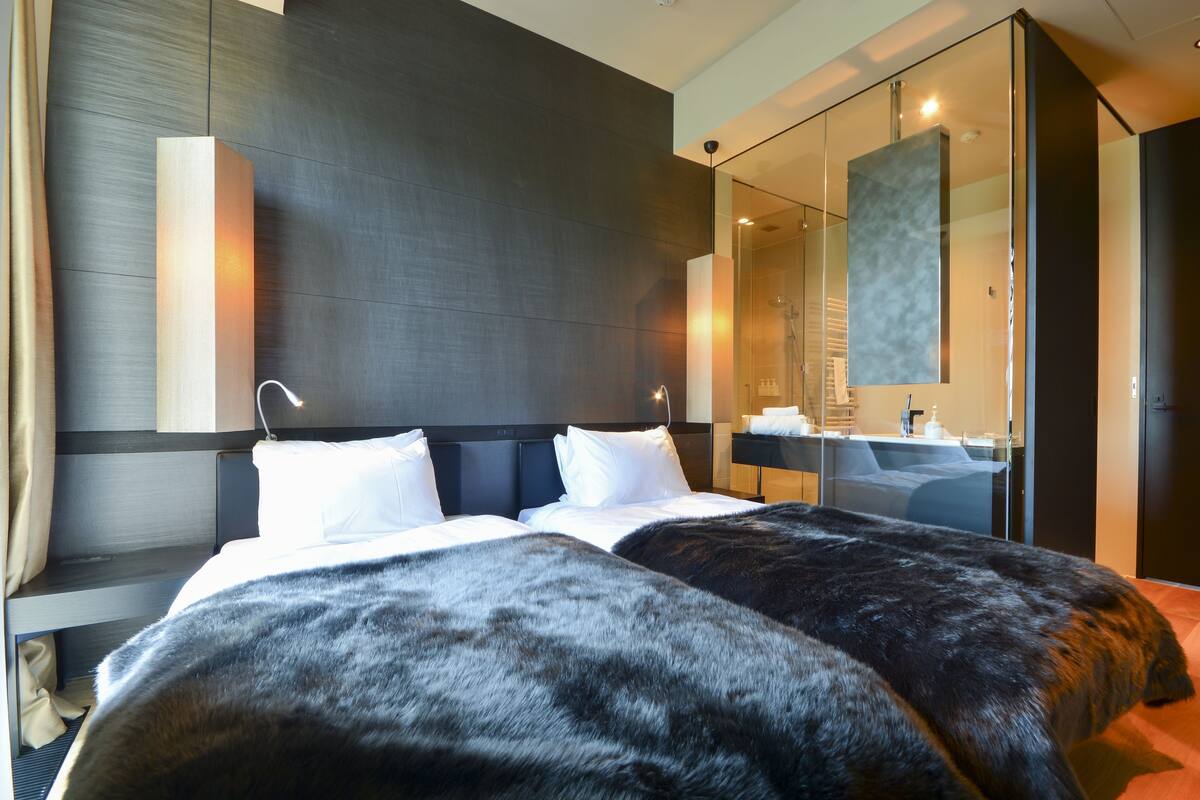 Una habitación de hotel moderna con una cama grande, un baño con ducha de vidrio y un espejo amplio.