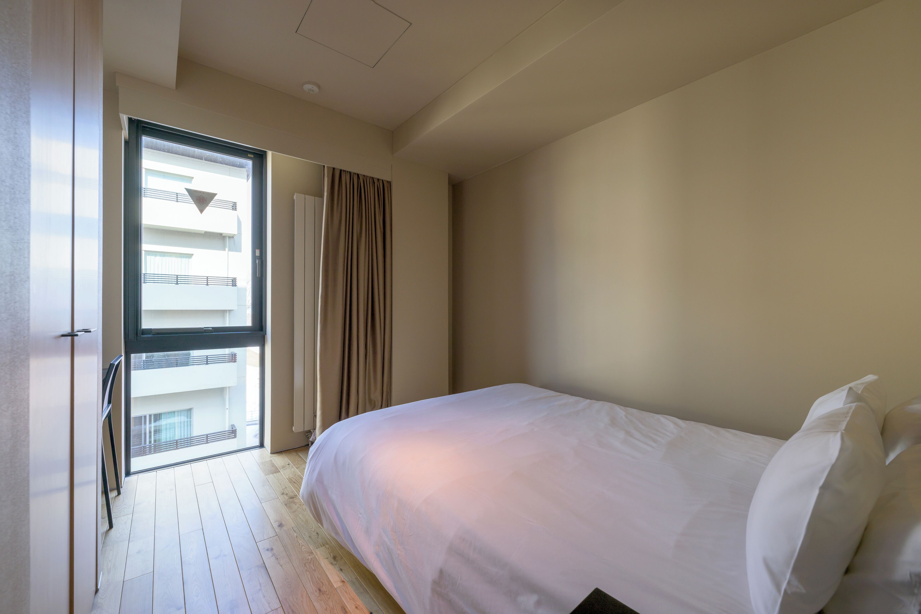 A bedroom with a large bed, a window with curtains, and a view of a balcony.
