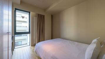 A bedroom with a large bed, a window with curtains, and a view of a balcony.