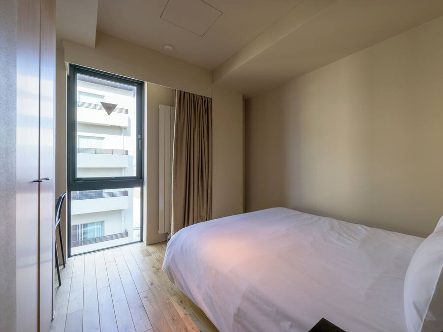 A bedroom with a large bed, a window with curtains, and a view of a balcony.