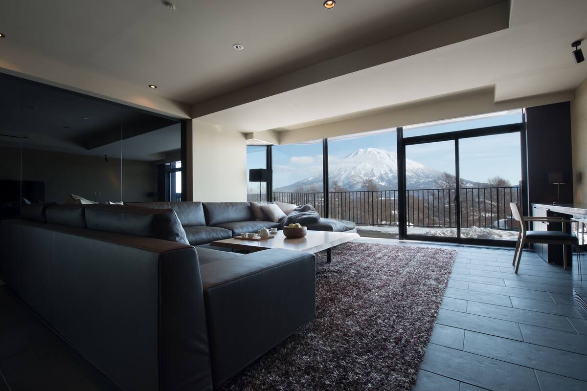 Una sala de estar moderna con un sofá seccional grande, una mesa de centro y vistas a una montaña nevada a través de amplios ventanales.