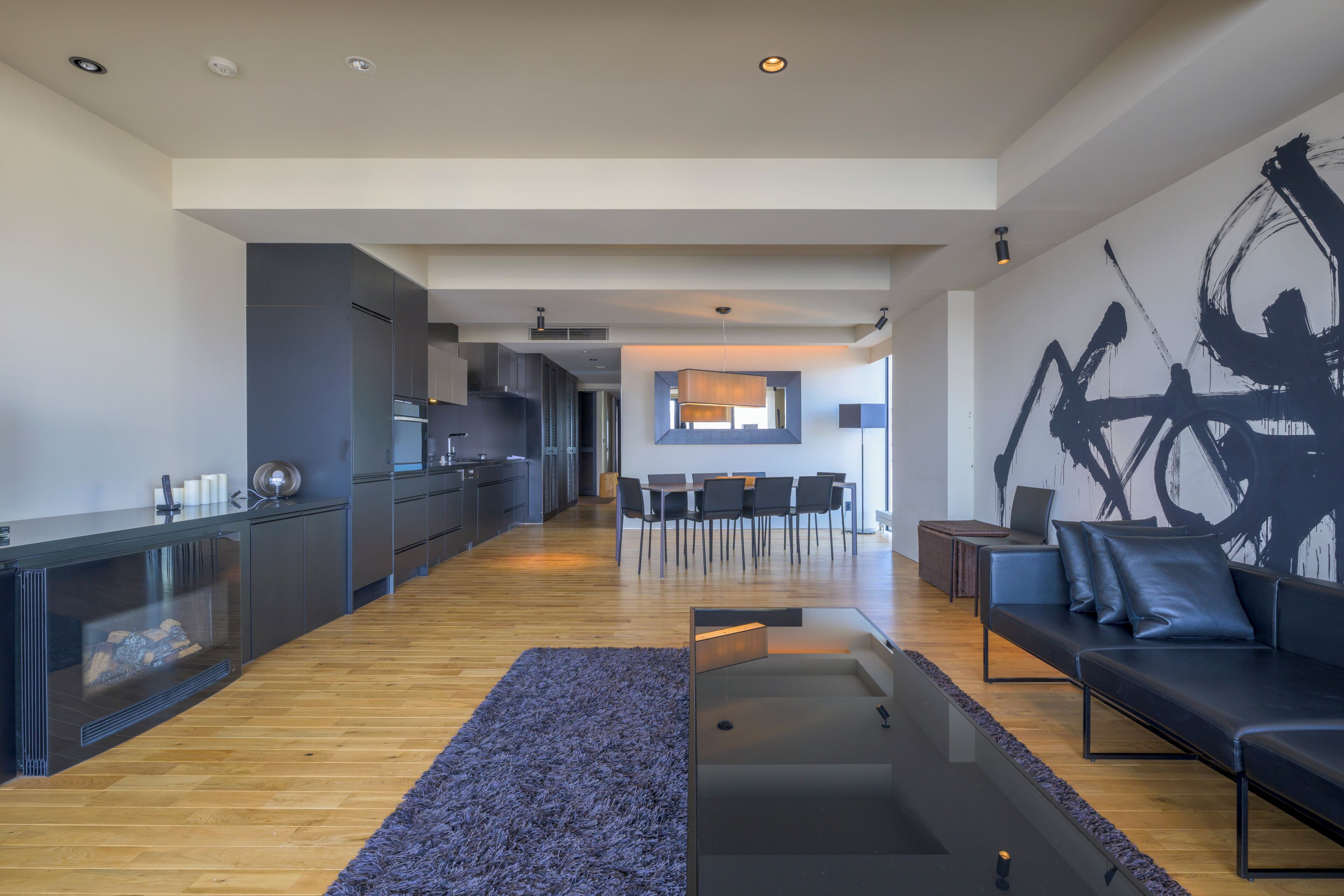 A modern living room with a sofa, a coffee table, and a dining area in the background.
