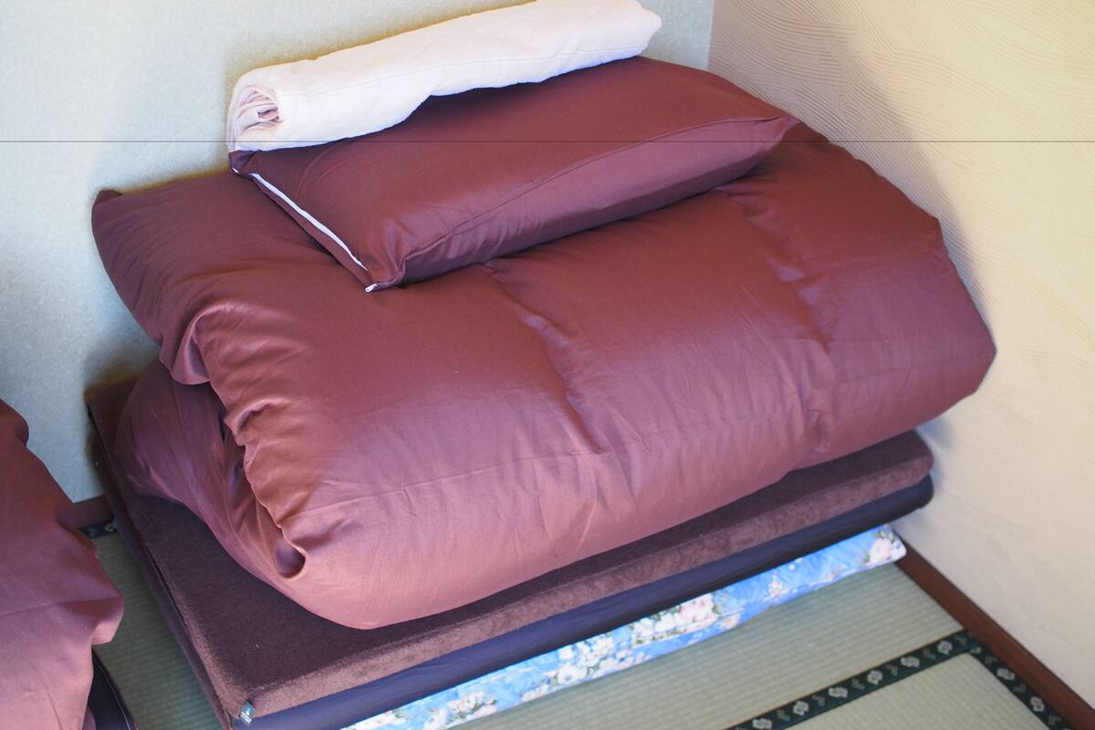 A bed with two large, dark-colored pillows and a folded white blanket.