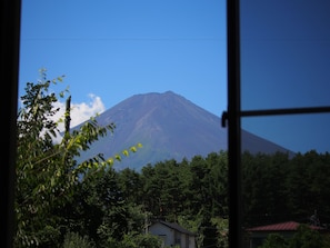A mountain with a clear sky, surrounded by dense forest and a few buildings. - Kikkake Green and Mt.Fuji - Hostel (Fujiyoshida)