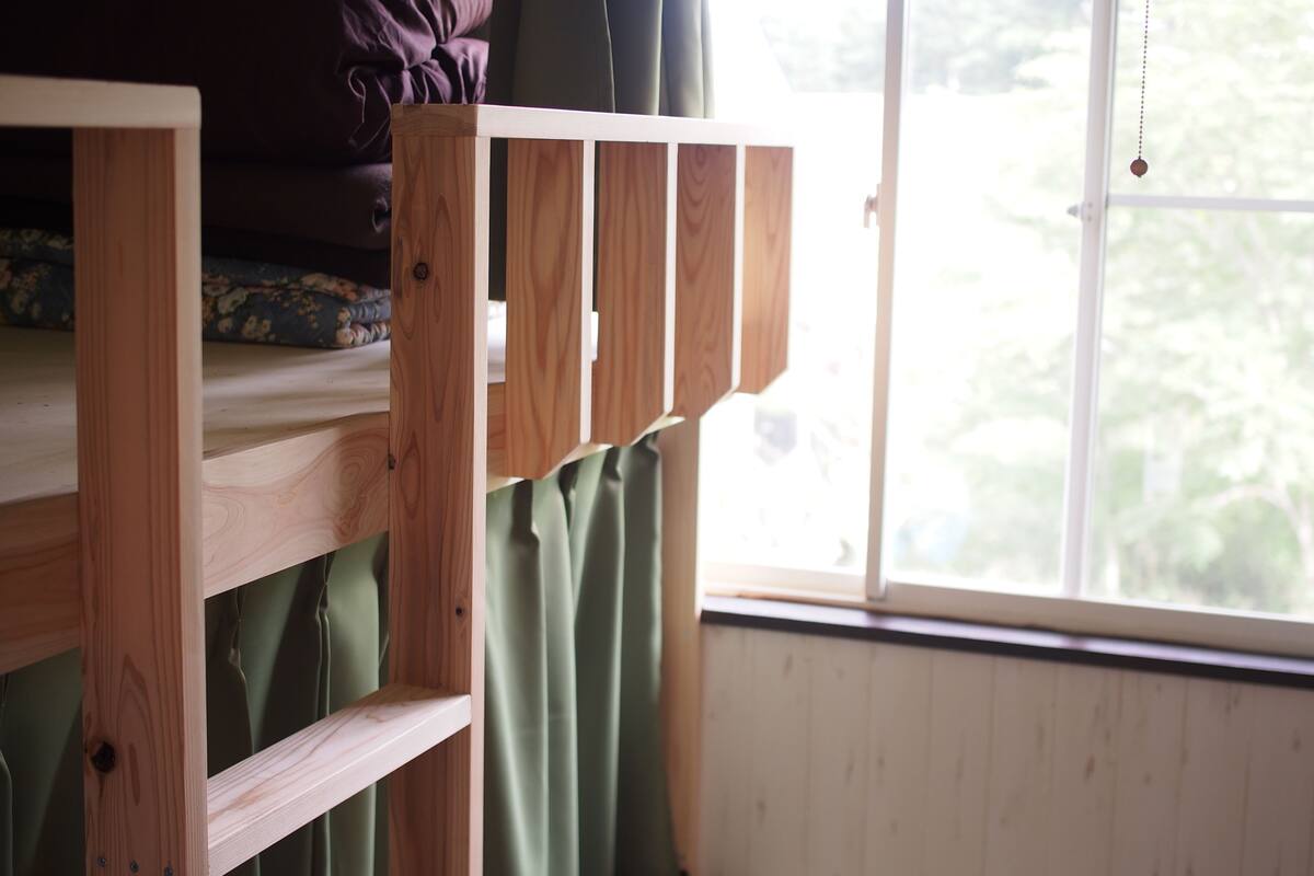 A bunk bed with a wooden frame and a window with a view of trees.