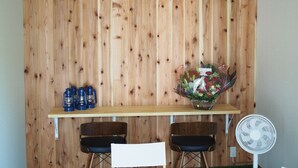 A room with a wooden wall, a clock, a fan, and a table with chairs and a flower arrangement. - Kikkake Green and Mt.Fuji - Hostel (Fujiyoshida)