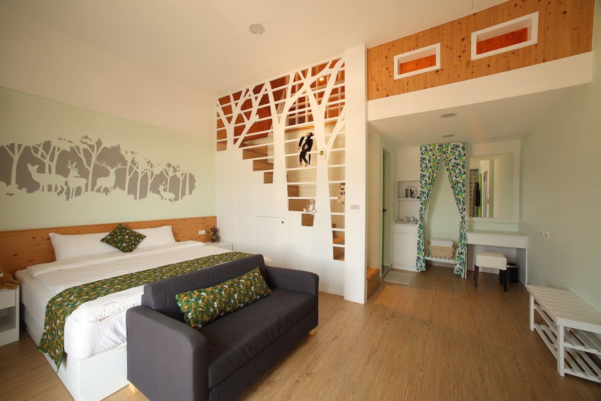 A bedroom with a bed, a sofa, a wooden staircase, a bathroom, and a mirror.