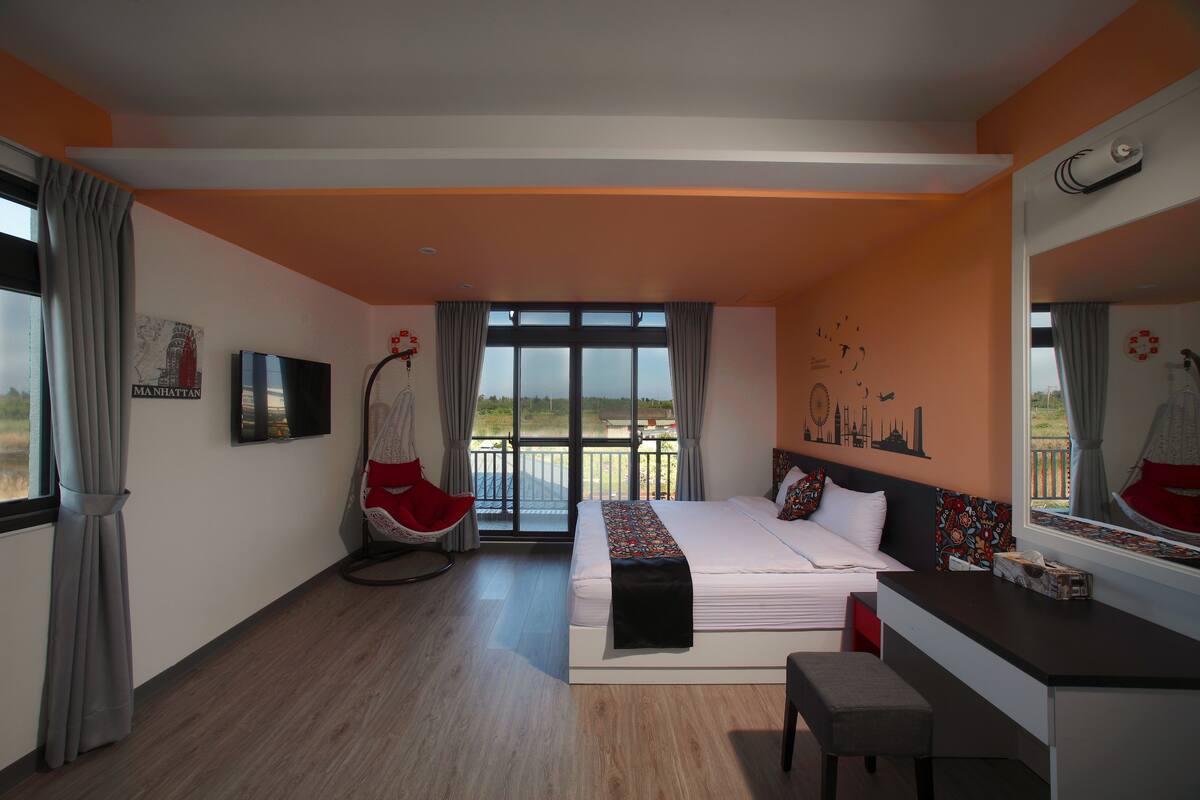 A modern hotel room with a large bed, a desk, a chair, and a balcony with a view.