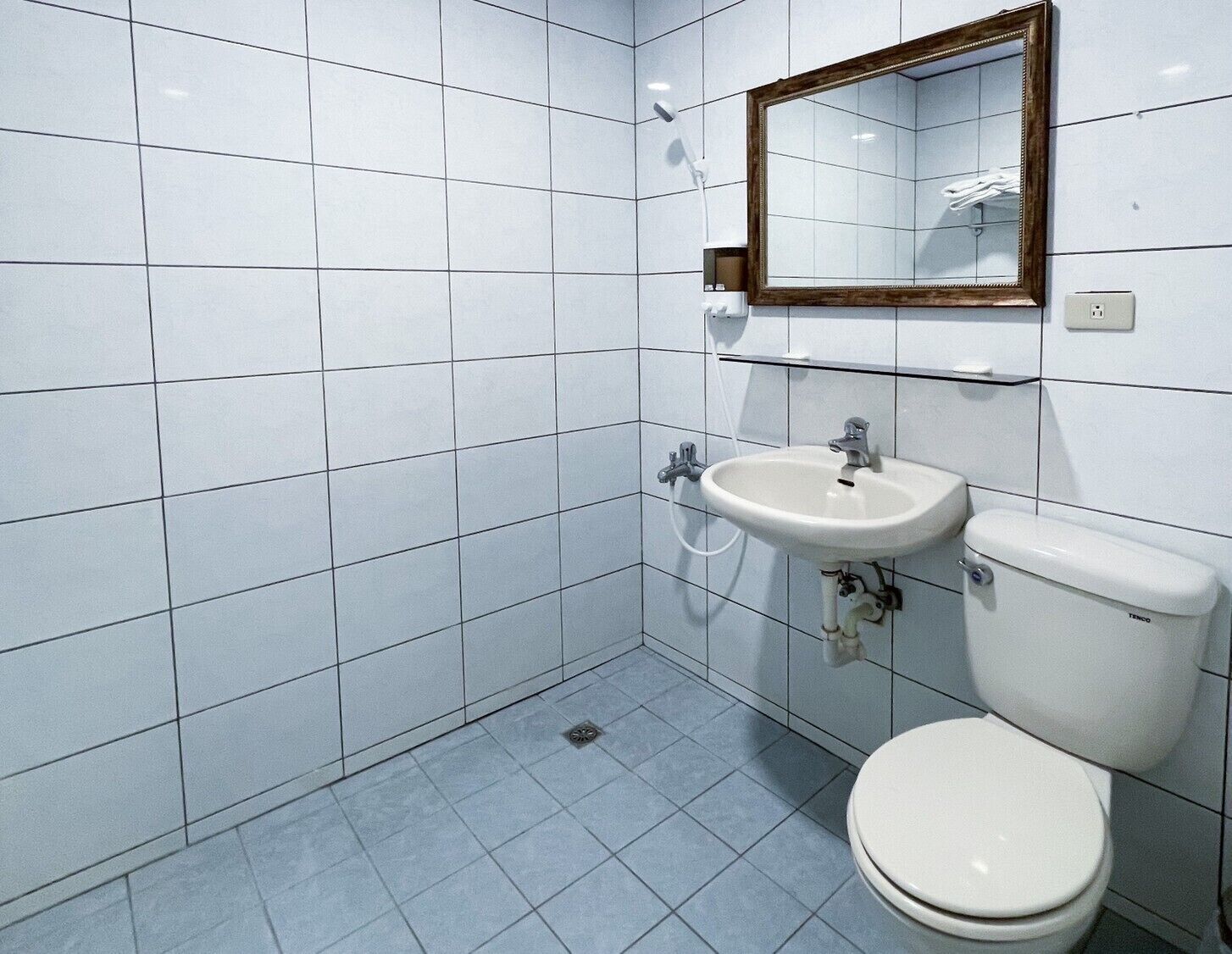 A small, modern bathroom with white tiles, a white sink, a toilet, and a mirror.