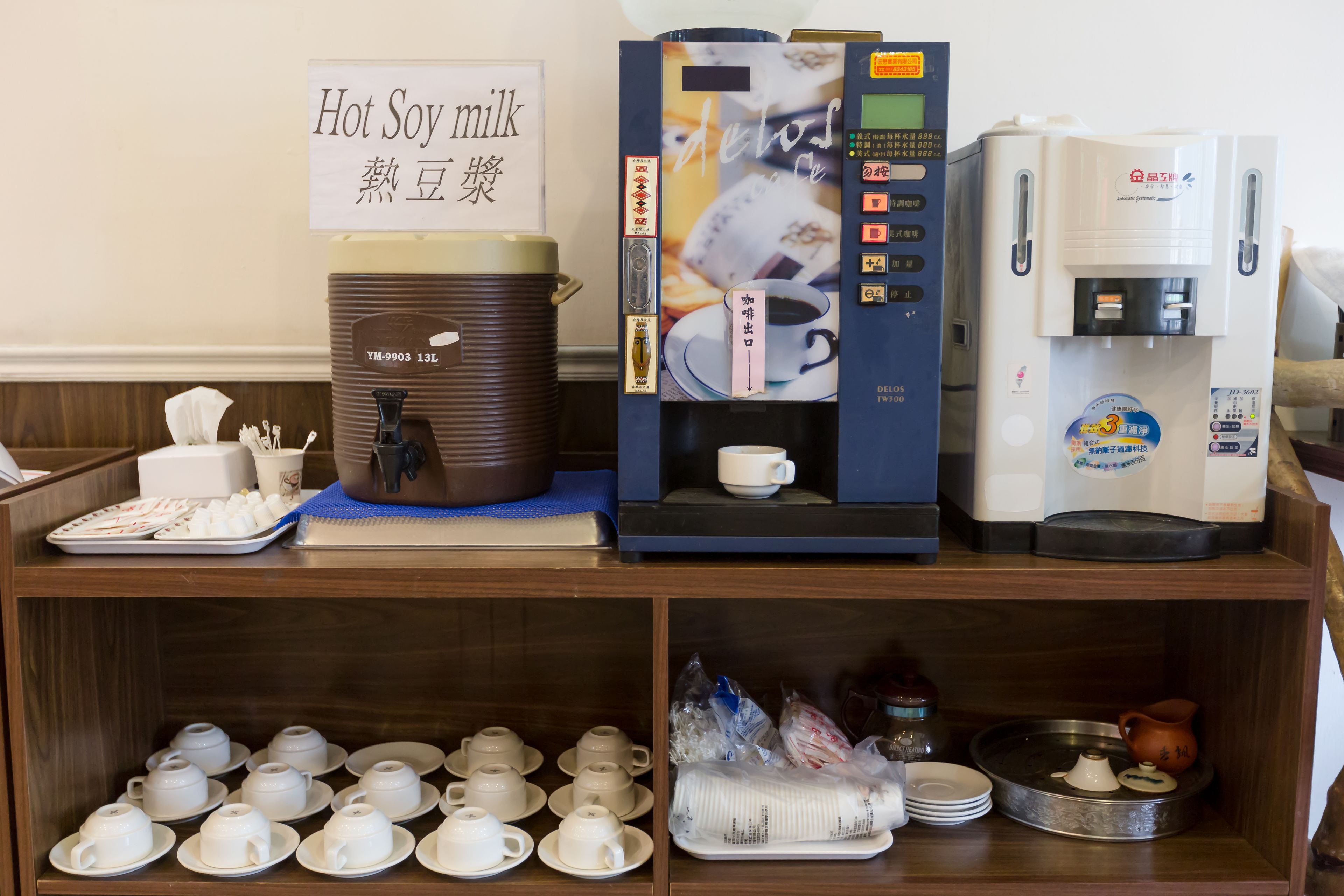 Una estación de café con dispensador de leche de soja caliente, una máquina de café y un dispensador de té.