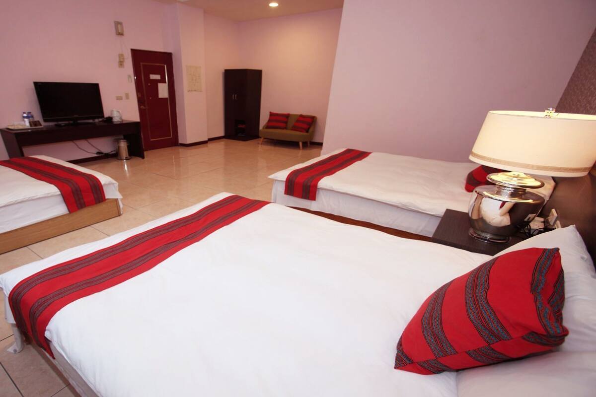 A hotel room with three single beds, a television, a desk with a computer, and a lamp.