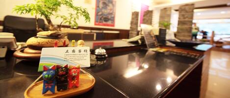 A reception desk with a plant, a telephone, and a card holder with cat figurines.
