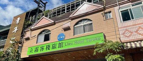 Un hotel con un letrero verde, un logotipo azul y un estilo arquitectónico tradicional.