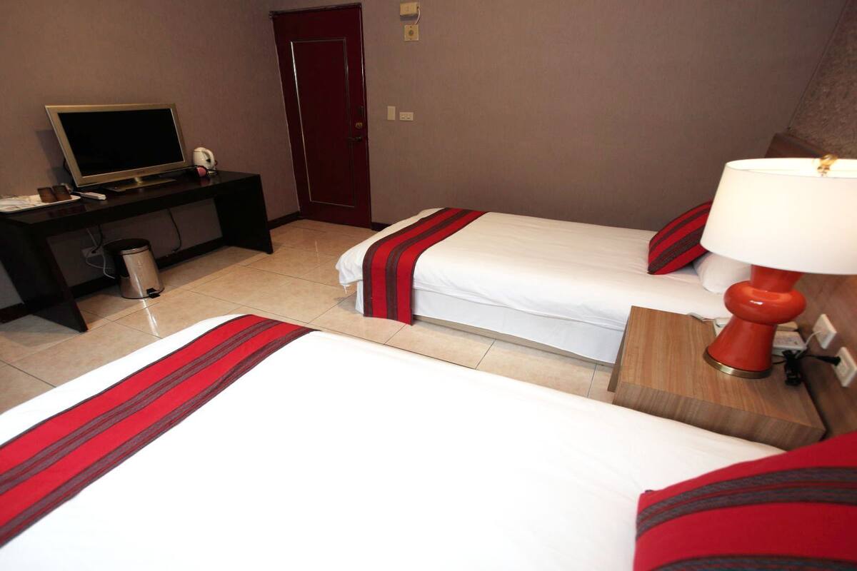 A hotel room with two beds, a desk with a computer, a lamp, and a trash bin.
