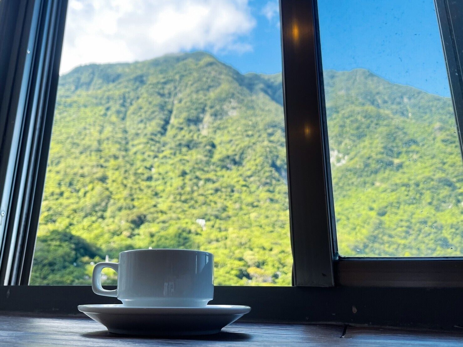 A cup and saucer on a table by a window with a view of a mountain.
