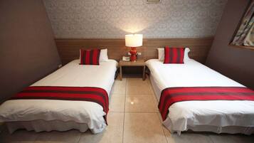 Una habitación de hotel con dos camas, cada una con una colcha a rayas rojas y blancas, una mesita de noche con una lámpara y un papel tapiz estampado en las paredes.