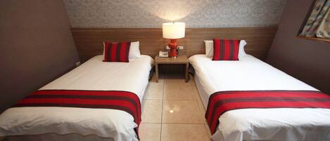 Camera d'albergo con due letti, ognuno con una coperta a righe rosse e bianche, un comodino con una lampada e carta da parati decorata sulle pareti.