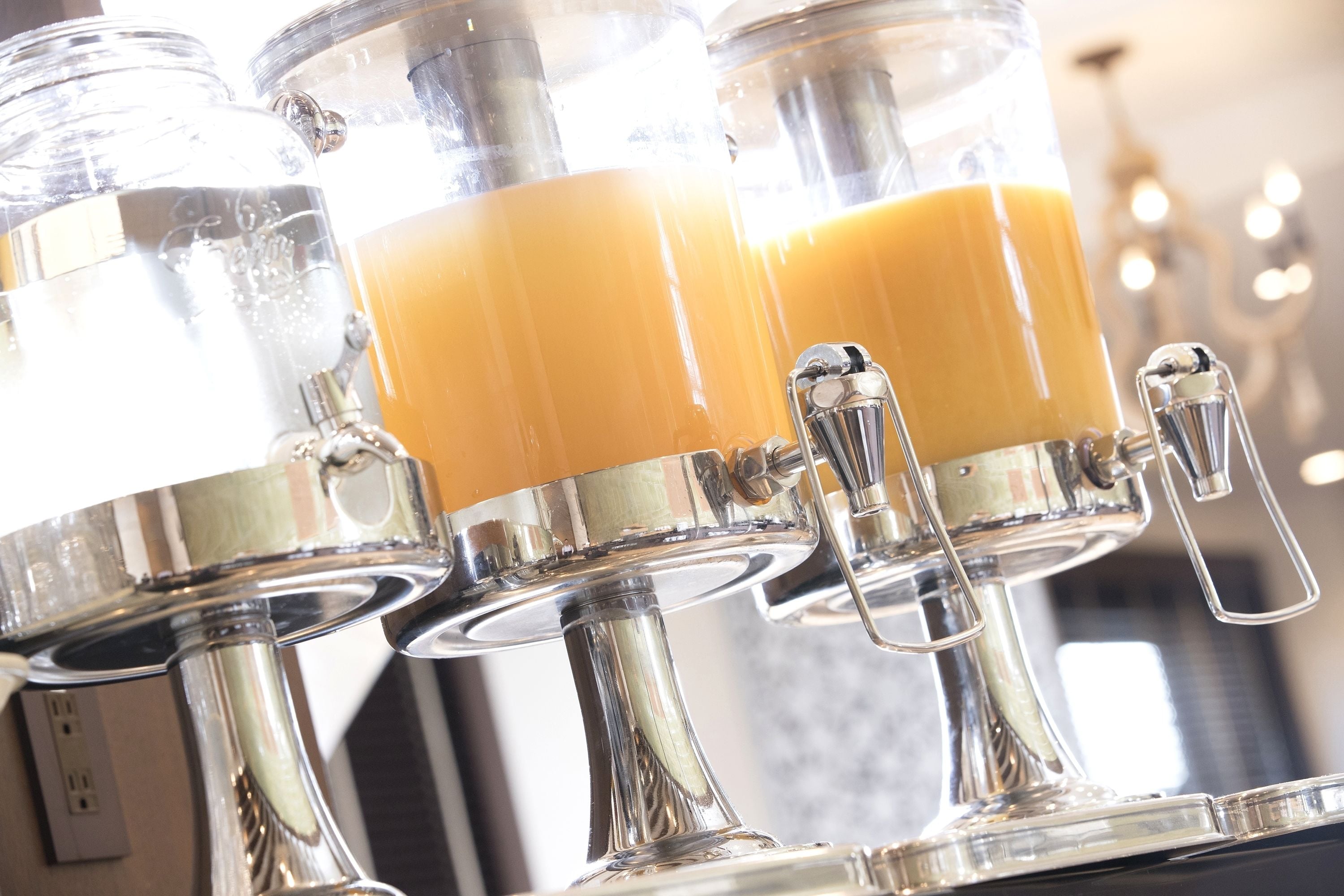 A juice dispenser with multiple spouts, each containing a yellowish beverage.