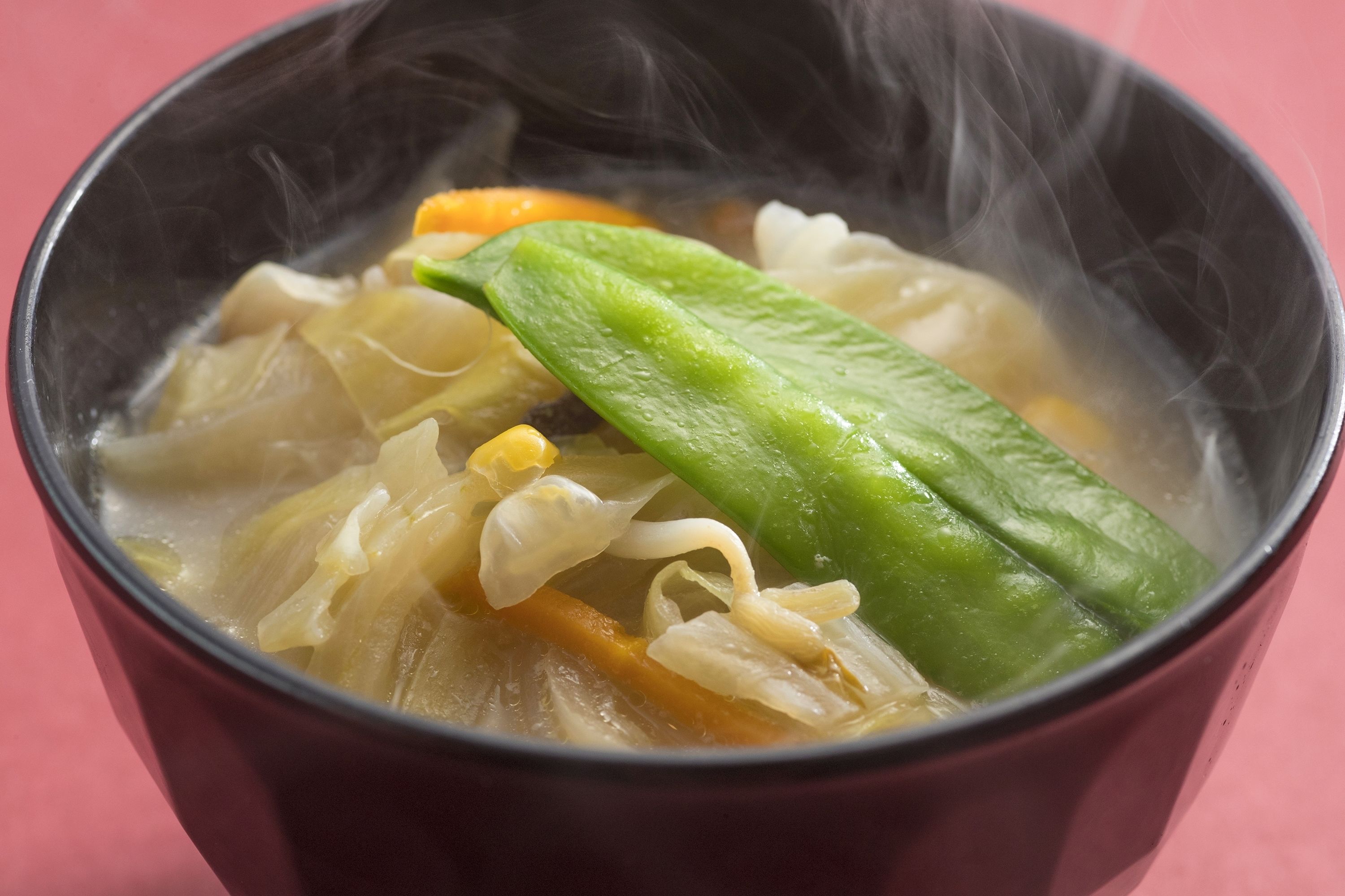 A bowl of soup with vegetables and steam rising from it.
