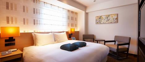 A hotel room with a large bed, two bedside lamps, a small table, a chair, and a painting on the wall.