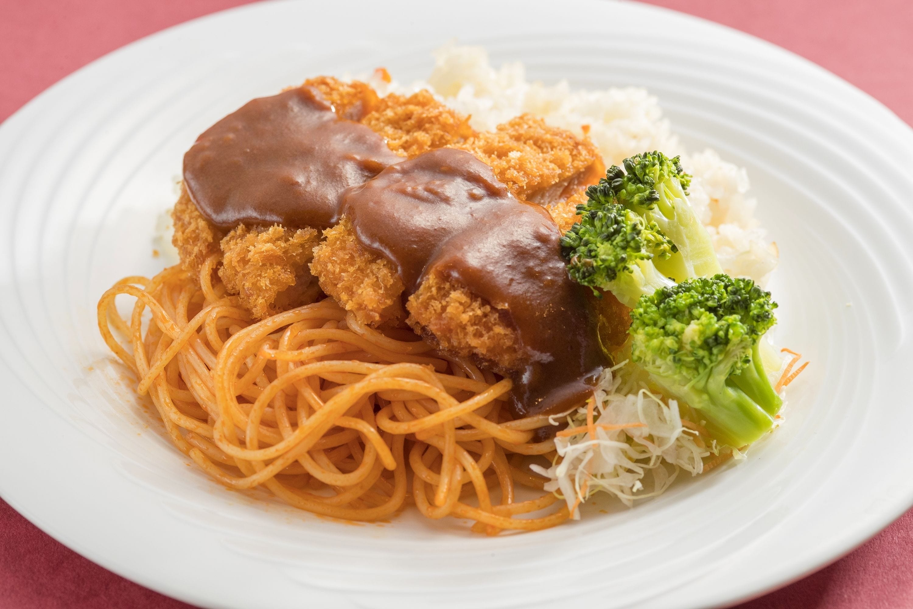 A plate of spaghetti with meatballs and a creamy sauce, served with broccoli and mashed potatoes.