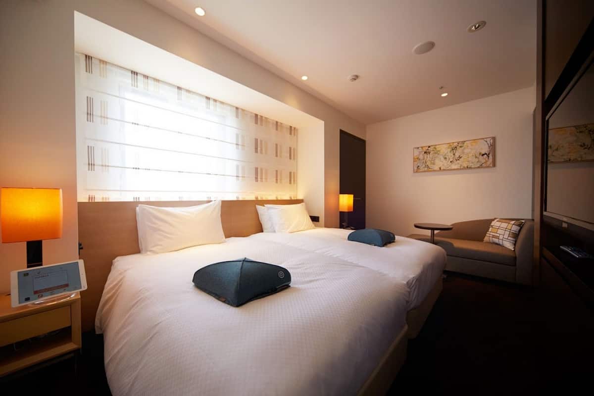 Quarto de hotel moderno com uma cama grande, mesas de cabeceira, um sofá e uma TV.