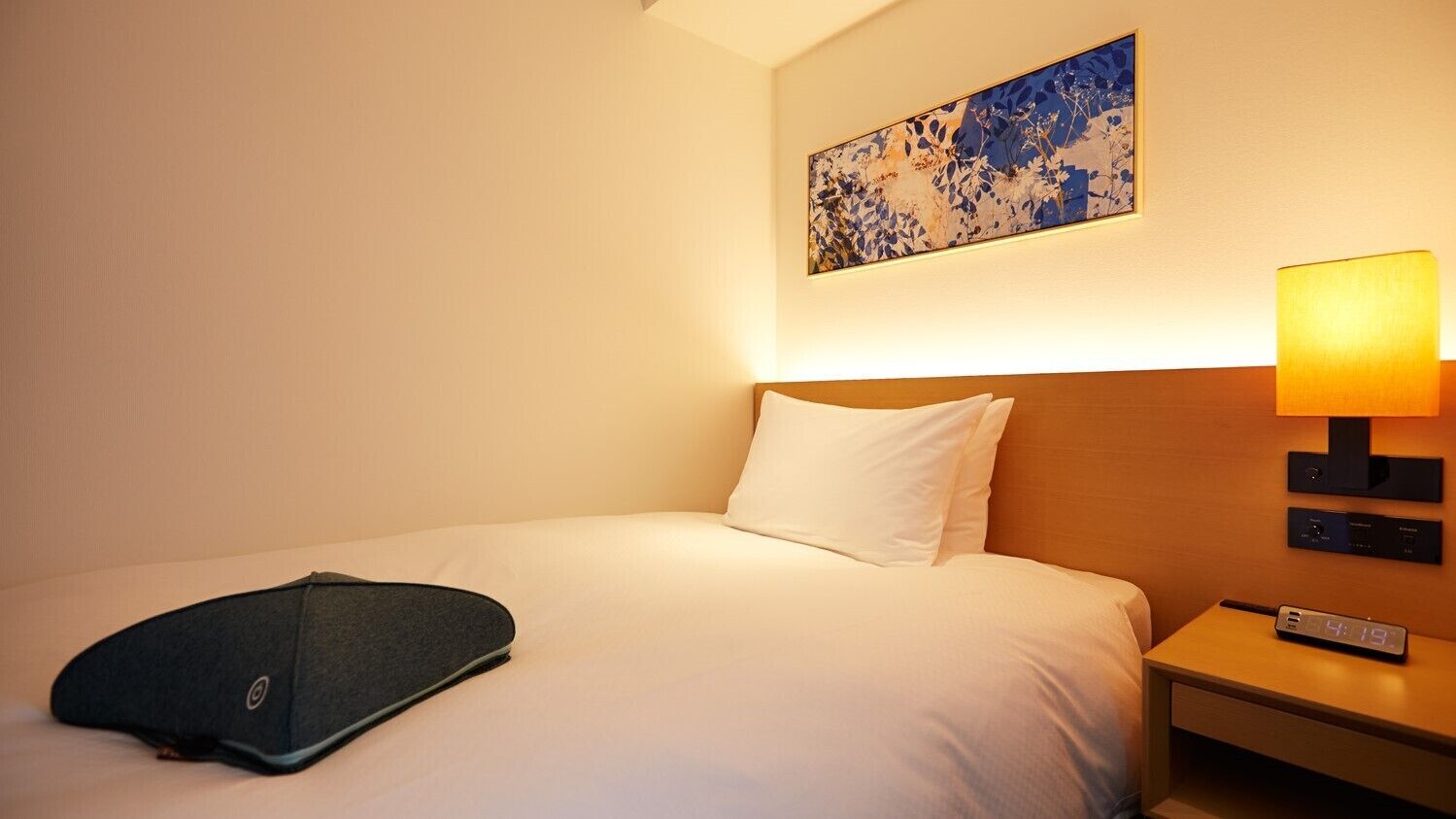 Ein Hotelzimmer mit einem Bett, einem Kopfkissen, einer Fernbedienung, einer Lampe und einer Uhr.