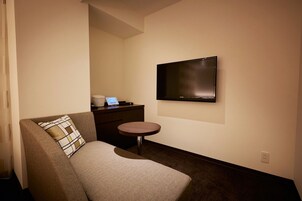 Una habitación de hotel moderna con sofá, una mesita redonda, un televisor de pantalla plana en la pared y un ordenador portátil sobre la mesa.