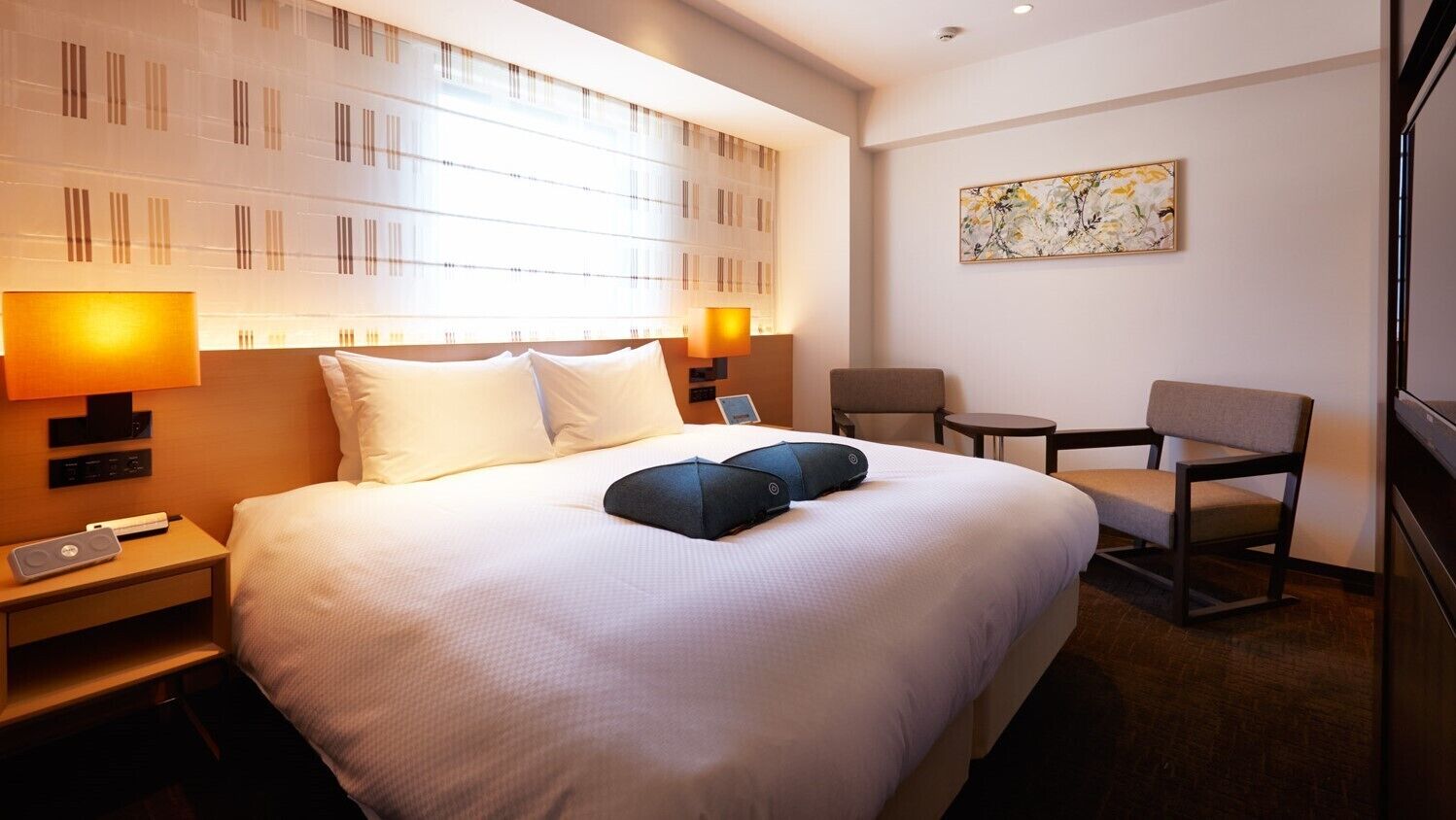Ein Hotelzimmer mit einem großen Bett, Nachttischlampen, einem kleinen Tisch und einem Sessel.