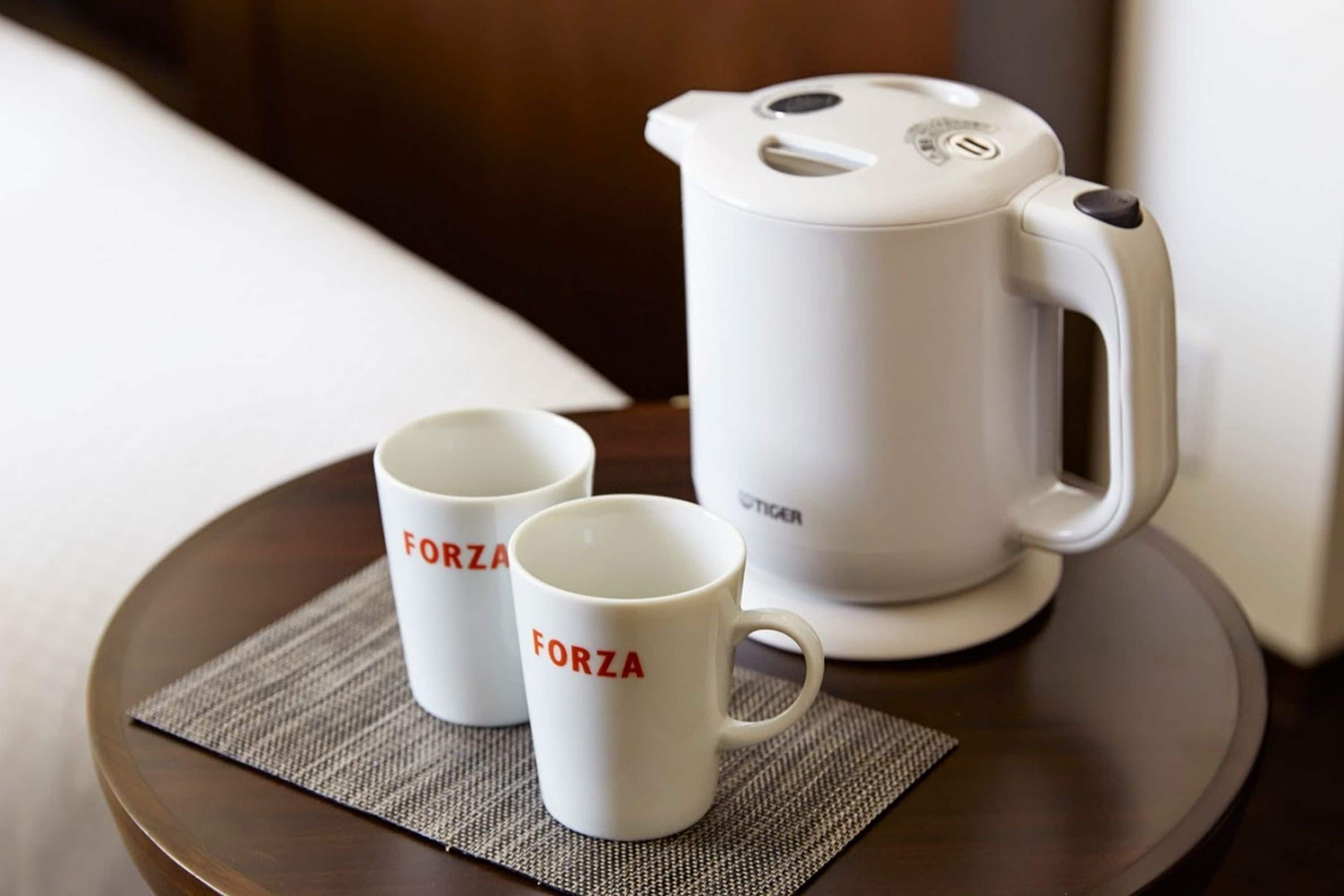 Dos tazas blancas con la palabra "FORZA" sobre una bandeja con una cafetera blanca.