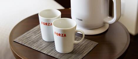 Dos tazas blancas con la palabra "FORZA" sobre una bandeja con una cafetera blanca.