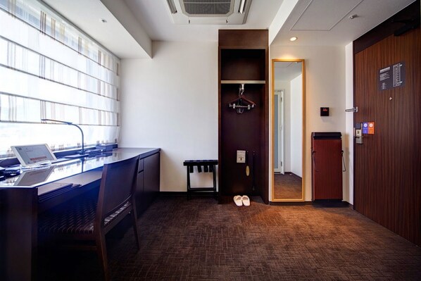 Una habitación de hotel con escritorio, ordenador portátil, zapatero y armario.