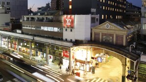 Un immeuble à plusieurs étages, sur lequel on peut voir une grande enseigne « HamaCross 411 », un magasin « Y! mobile » et une station de tramway avec un passage piéton.