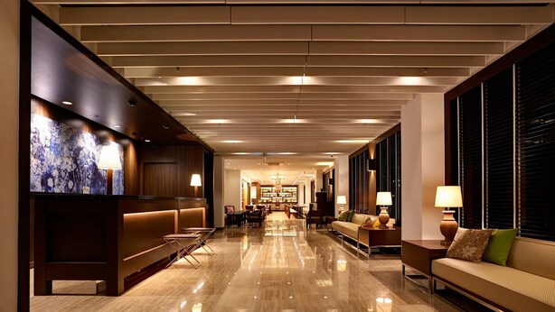 Un hall d’hôtel spacieux, doté d’un sol ciré, de coins salon et d’un lustre central.