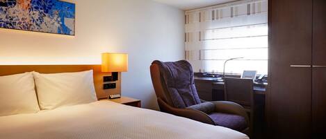 A hotel room with a bed, a chair, a desk, and a window with blinds.