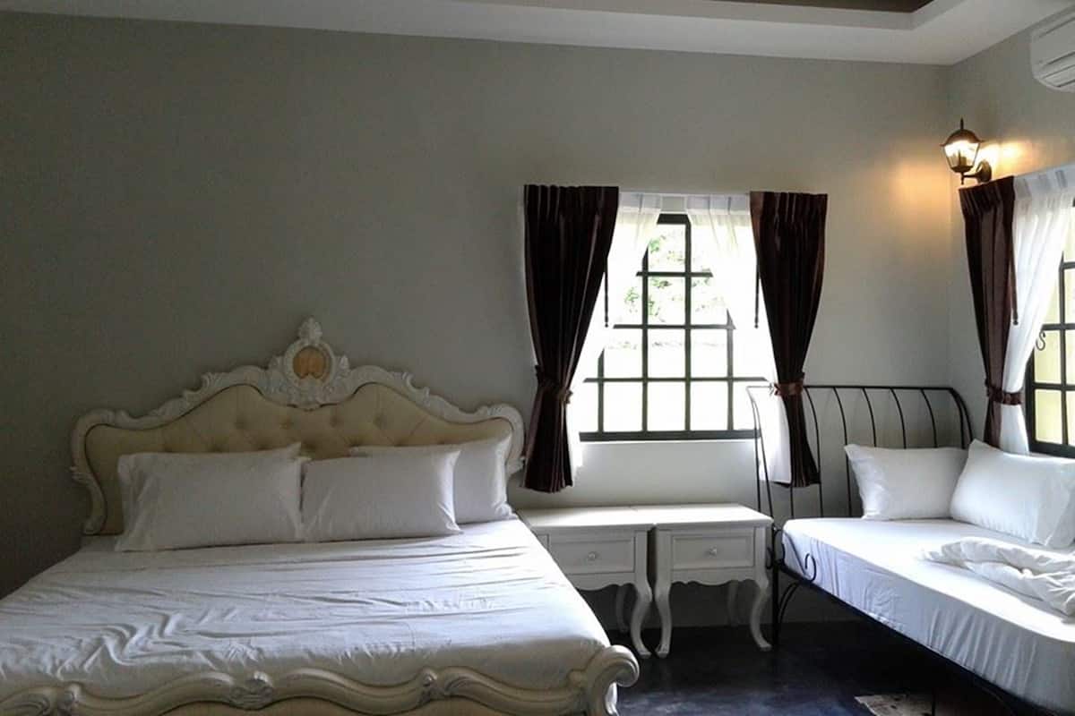 A bedroom with a large bed, two bedside tables, a window with curtains, and a wall-mounted light fixture.