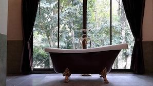 Uma banheira em um quarto com uma janela grande, piso ladrilhado e borda de pedra.