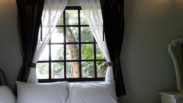Quarto com cama, cortinas brancas e janela com vista para árvores.