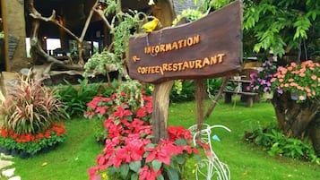 A sign for a coffee restaurant surrounded by lush greenery and flowers.