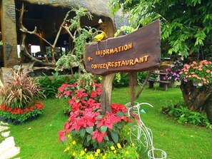A sign for a coffee restaurant surrounded by lush greenery and flowers. - Timberland and Fruit Resort (Suan Phueng)