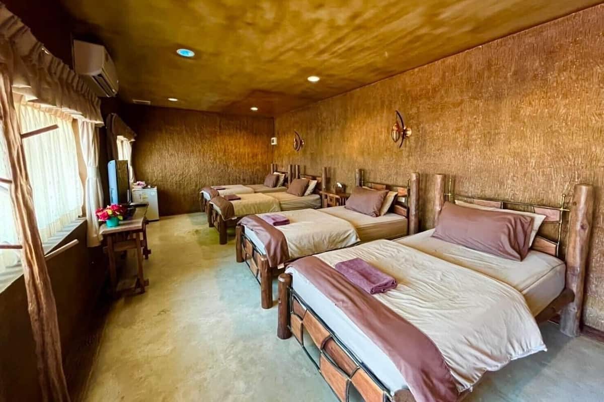 A room with four wooden beds arranged in a row, a small desk with a computer, and a window with curtains.