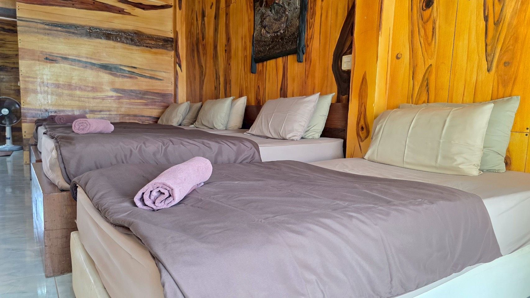 Quarto de hotel com duas camas, cada uma com uma toalha enrolada, e painéis de madeira nas paredes.